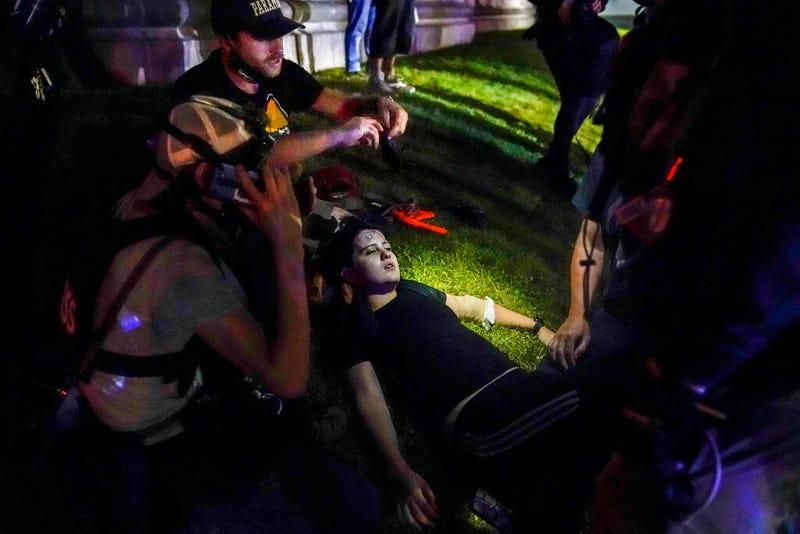 FILE- In this Aug. 25, 2020 file photo, Gaige Grosskreutz, top, tends to an injured protester during clashes with police outside the Kenosha County Courthouse in Kenosha, Wis. Grosskreutz who was shot in the arm by Kyle Rittenhouse during street protests in Kenosha last year has filed a federal lawsuit that accuses police of enabling the violence by allowing armed militia to roam freely during the demonstration.