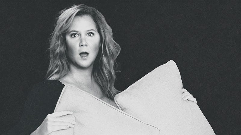 Amy Schumer holding 2 pillows with surprised look