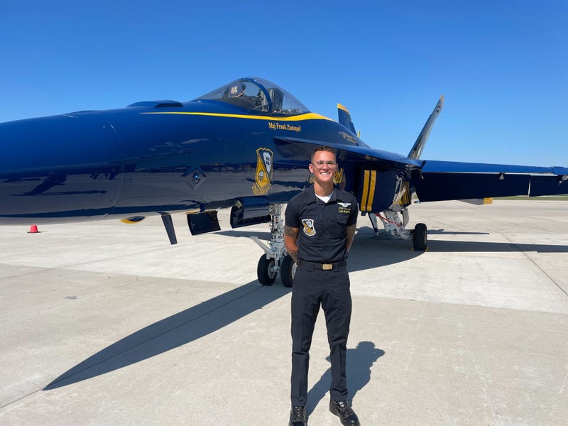 A young man stands in front of an airplane