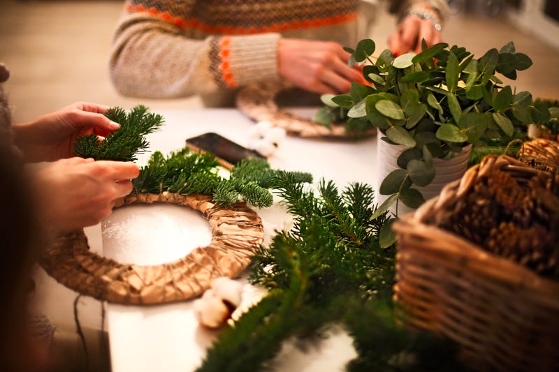 The hands of two unseen people arrange garlands on Christmas wreaths