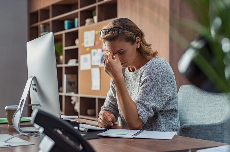 A woman sits at a computer squeezing her nose in frustation