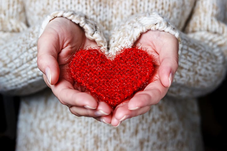 Girl in a light sweater gives a knitted heart