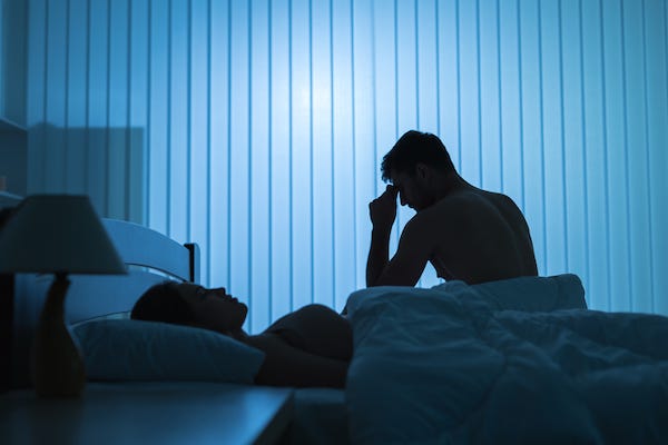 Man sitting in bed with head on hand