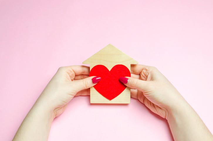 A girl holds a house and heart in her hands.