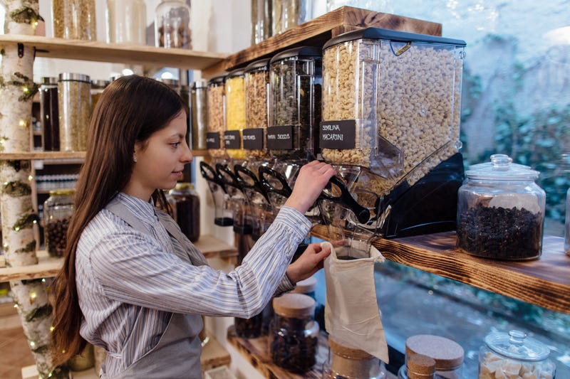 A woman uses a reusable bag to get noodles from a bulk dispenser