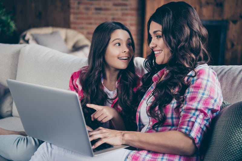 A mother and daughter happily use a laptop