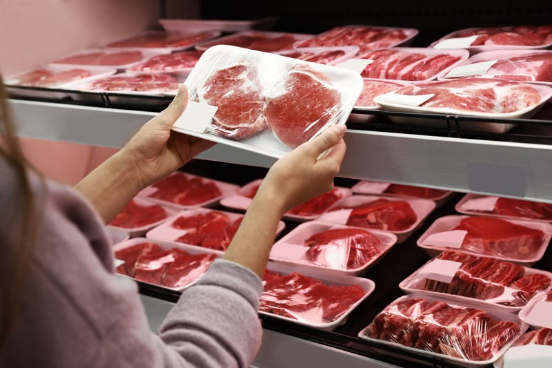Woman taking packed pork meat from shelf in supermarket
