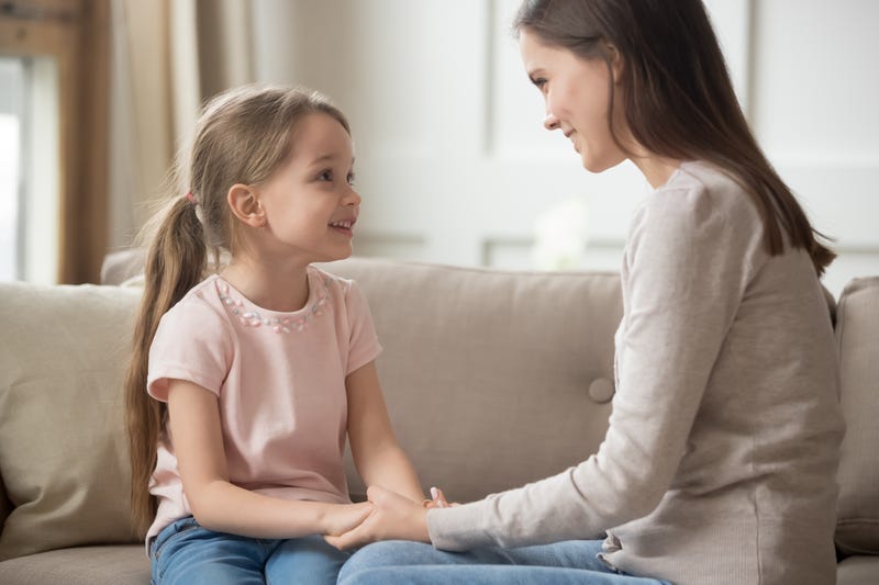 A mother and young daughter sit on a couch talking