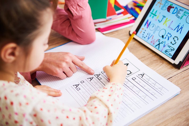 A kid traces letters while her mom helps with a tablet app
