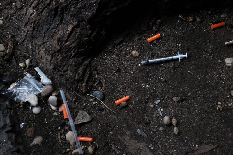 Hypodermic needles litter the ground.