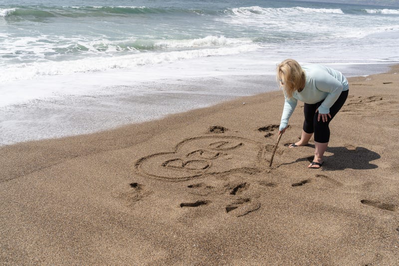 Blonde woman writes Bae (slang for Before Anyone Else, representing a romantic relationship) in sand on the beach