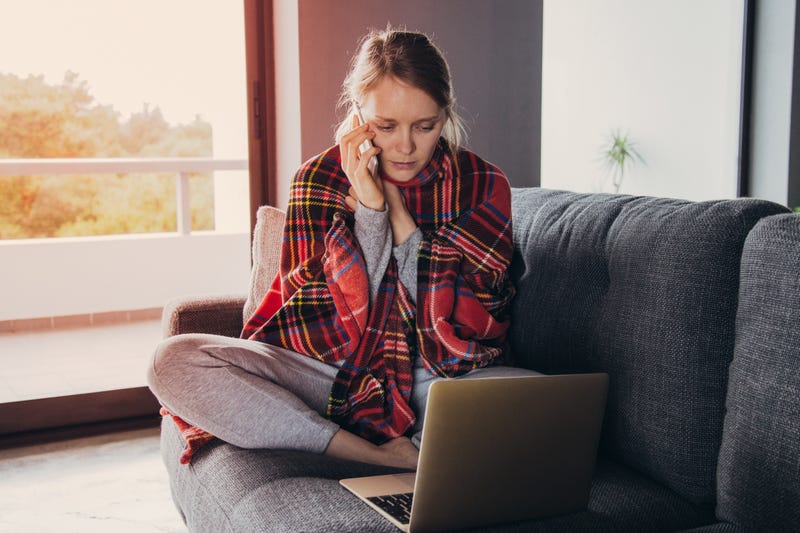 A sick woman uses a laptop on her couch