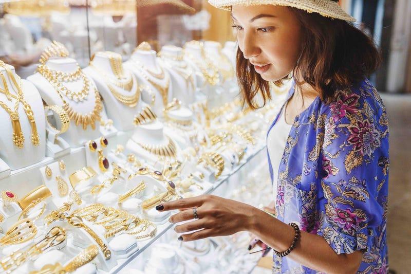 A woman stands over a jewelry case picking out a piece