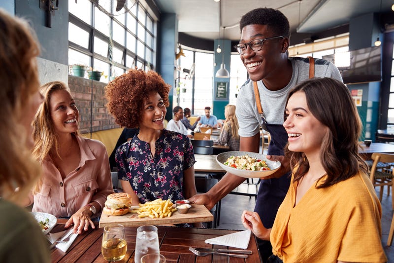A group of friends sits around a table as a waiter brings food