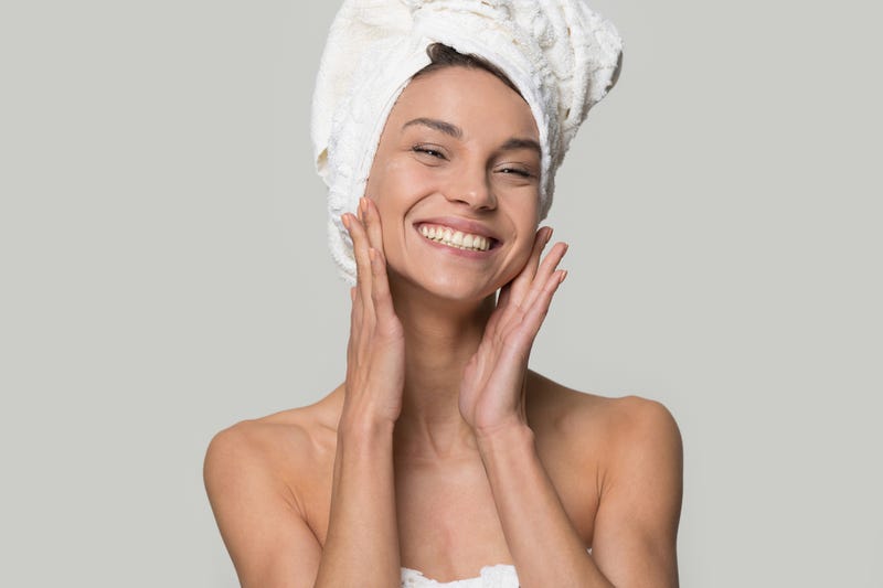woman with white towel on head after shower having toothy smile touch gently healthy shiny clean skin