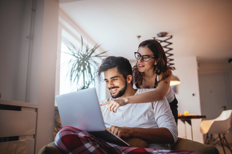 A woman leans over a man's shoulder pointing at his computer screen