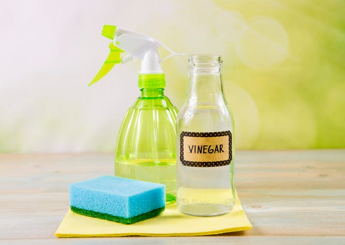 A spray bottle beside a sponge and a bottle labeled "vinegar"