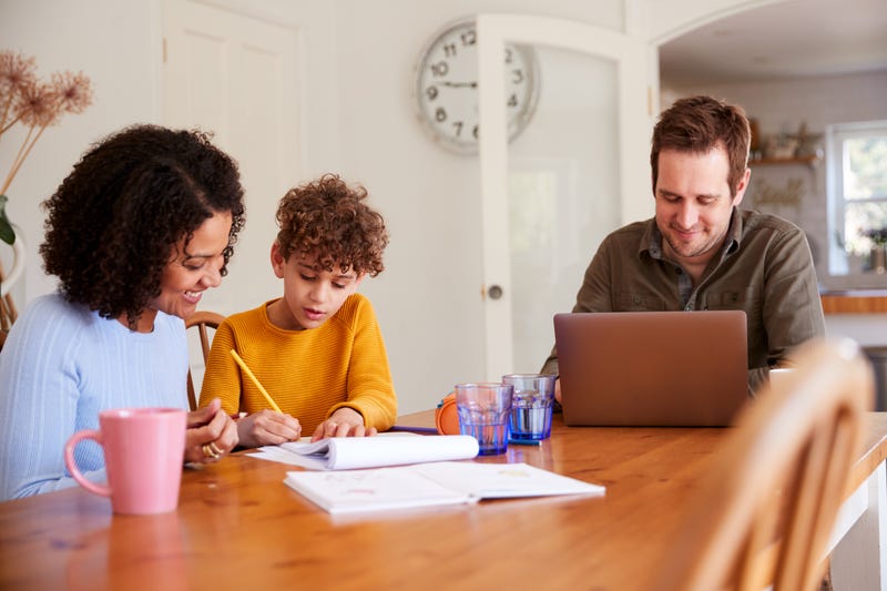 Two adults sit at a table, one working, while helps a child do work