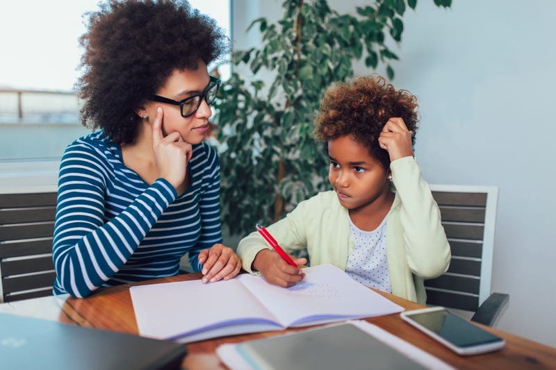 A kid works on homework while a mother looks on