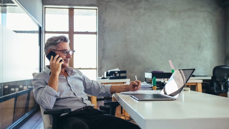 A man leans back in his chair on the phone while working