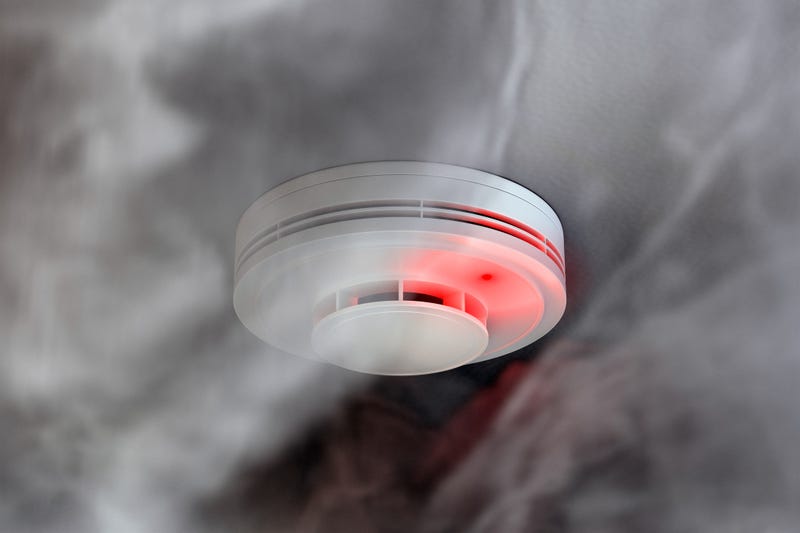 White plastic fire alarm smoke detector with red LED indicator on ceiling
