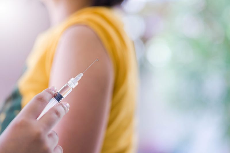 Vaccination stock phot. Needle in foreground, woman in yellow shirt in background.