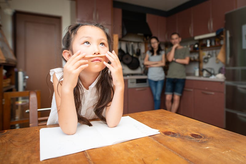 A girl looking bored with work as her parents look on from the background