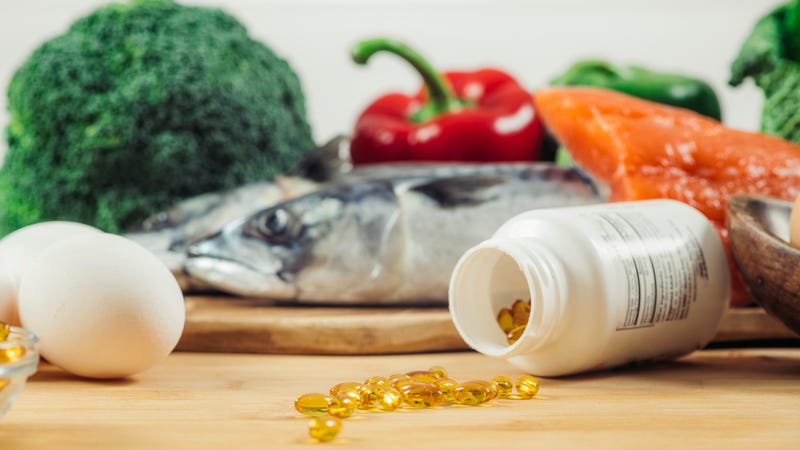 Supplement Bottle with Gel Capsules On a Wooden Table. Natural Food Sources of Vitamin D In Background.
