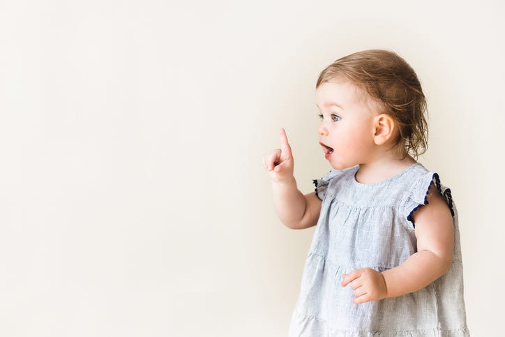 Baby girl pointing her finger, excited and emotional, on neutral background