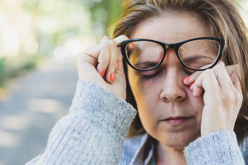 A woman lifts her glasses to rub her eye