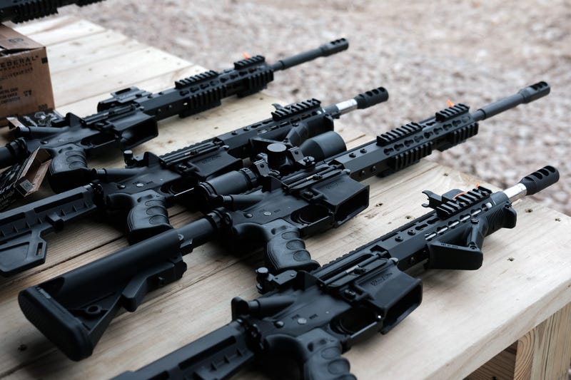 AR-15 rifles and other weapons are displayed on a table at a shooting range