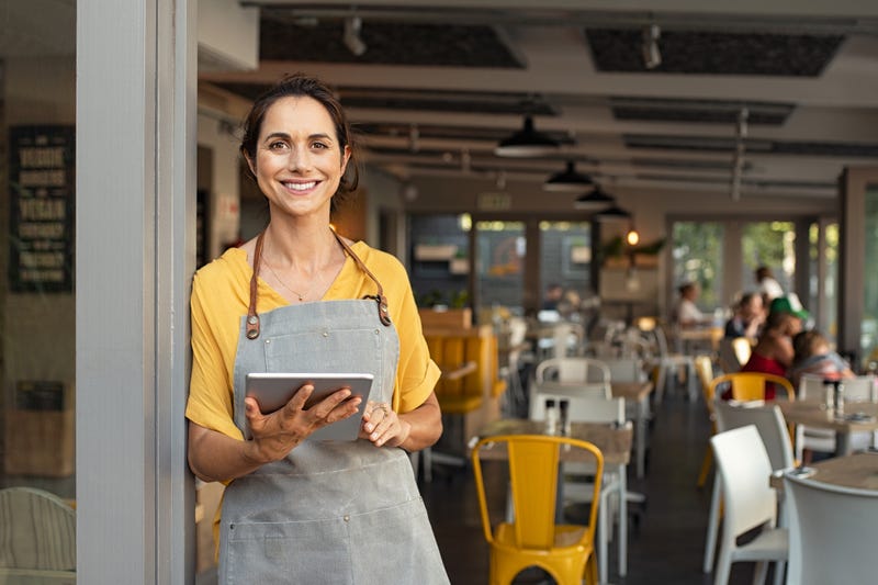 A woman stands in the doorway of a restaurant with a tablet