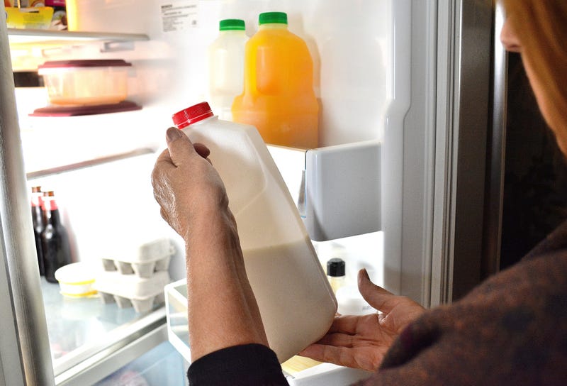 A woman holds a carton of milk in front of an open fridge