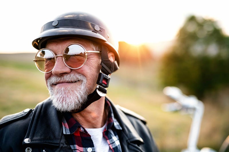 An old man in mirrored sunglasses and a helmet stands in front of a motorcycle