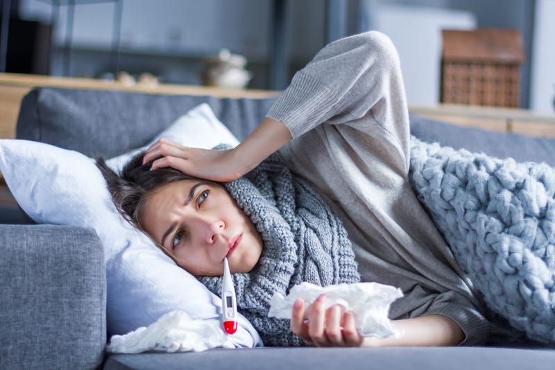 A woman lies on a couch with a thermometer and used tissue