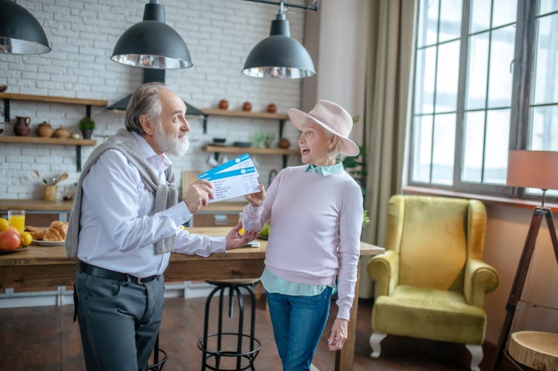 Making a surprise. A senior man presenting boarding passes to his wife