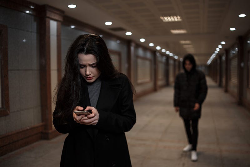 a young beautiful woman walks through an underground passage at night, followed by a man in dark clothing with a hood on his head. a woman tries to dial the number of the rescue service on the phone