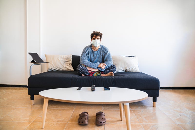 Young man sits on the couch while wearing face mask