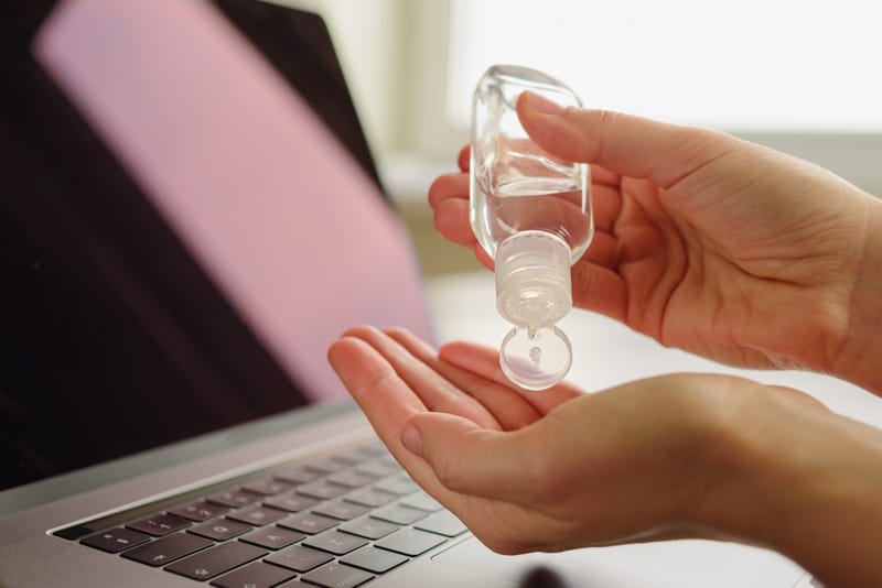 A person using hand sanitizer above a laptop