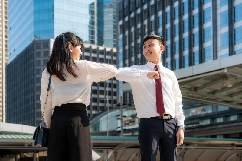 Two workers in business attire bumping elbows