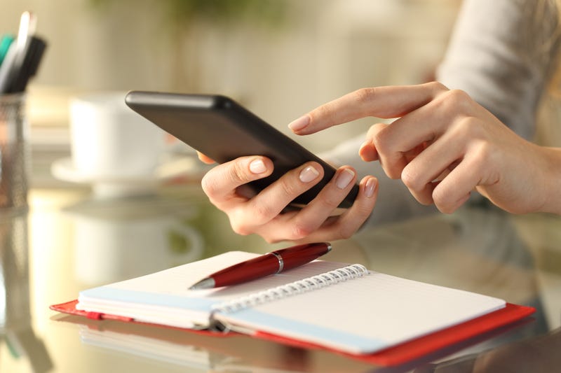 Close up of a woman's hands checking smart phone with personal organizer diary or agenda over the table at home.