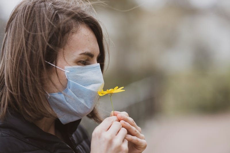 woman smelling flower through face mask
