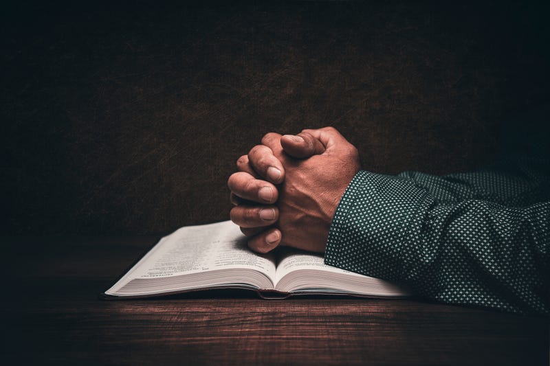 The hands of a church pastor praying over an open bible in his desk.