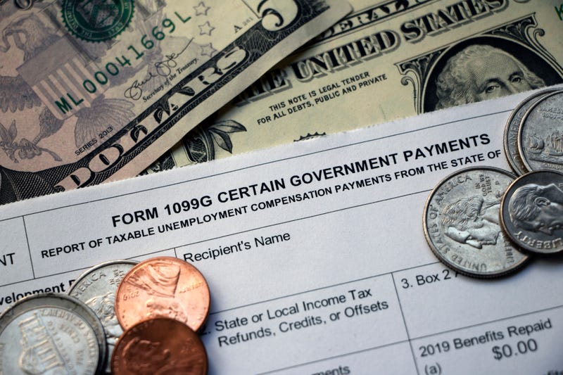 Closeup of the top of a tax Form 1099G Certain Government Payments - Taxable Unemployment Compensation Payments on top of cash with some coins scattered on top.