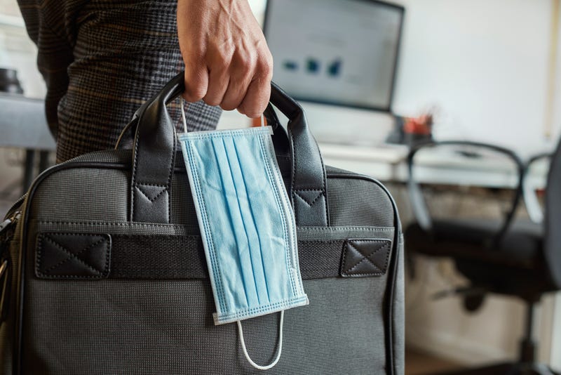 Person holding laptop case and face mask in an office