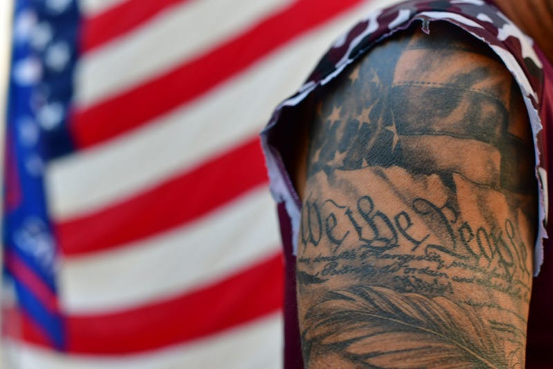 A tattoo reads "We the People"