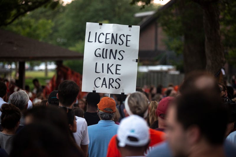 Highland Park shooting vigil, person holds sign reading "License guns like cars."