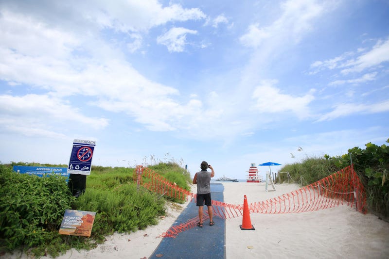 A man takes a photo of the beach next to fencing indicating that the beach is temporarily closed in South Pointe park on July 4th in the South Beach neighborhood of Miami Beach, Florida