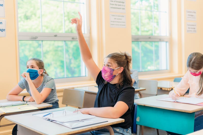 A girl wearing a mask raises her hand in class.
