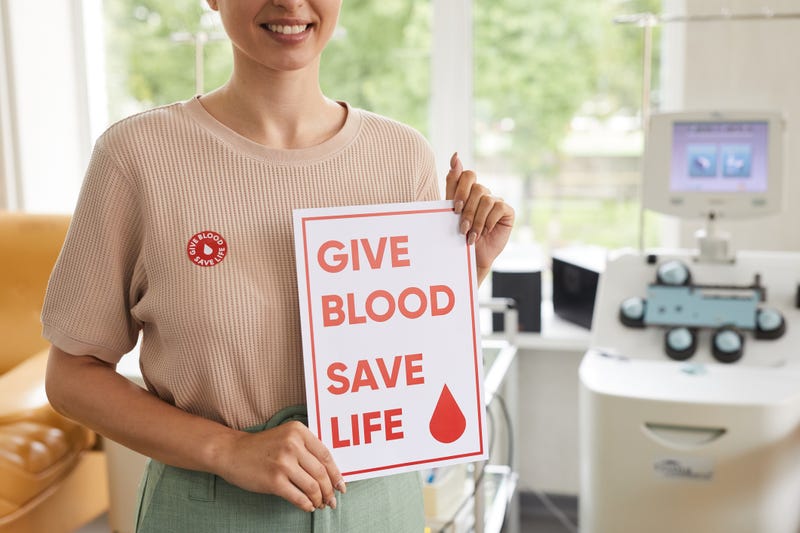 A woman holds a sign that reads "give blood, save a life"